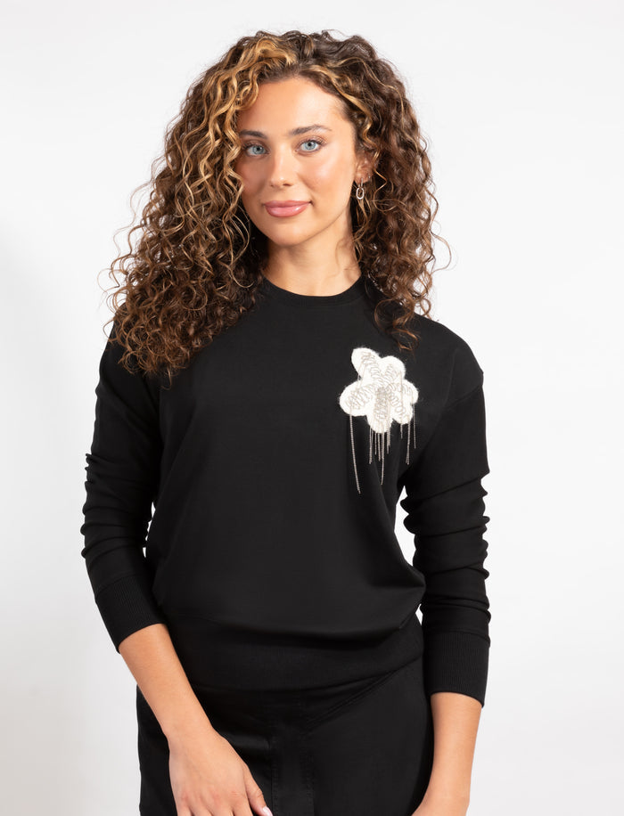 Black long-sleeve top with crew neck and white floral applique at left chest