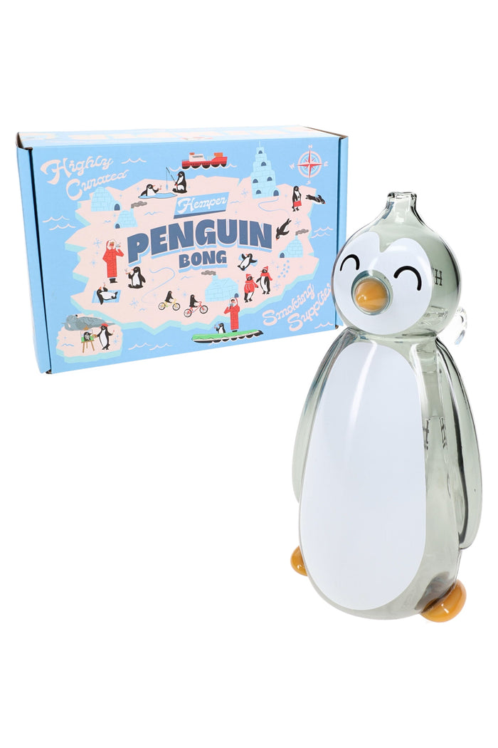 Smiling Hemper penguin glass bong posed beside its blue Penguin Bong box, angled product shot showing beak mouthpiece and compact glass water pipe.