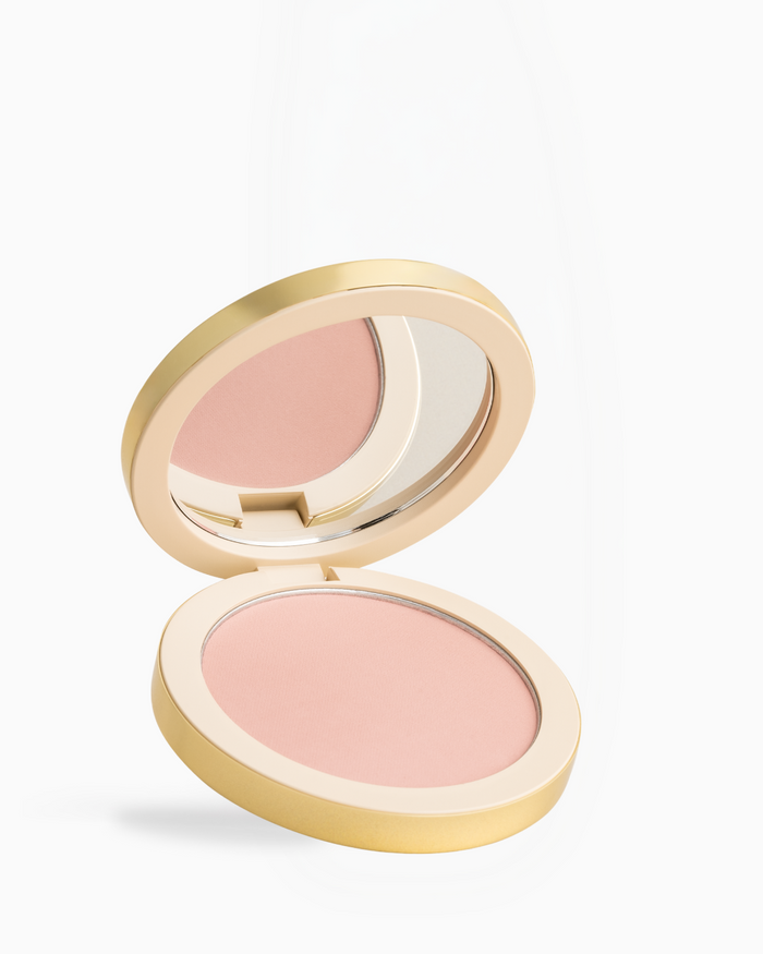 An open round makeup compact with a gold-toned case and a light pink pressed powder, shown on a clean white background.