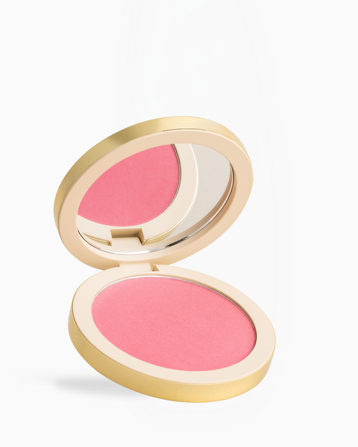 An open round blush compact with a gold-toned case, showing a vibrant pink pressed powder blush and an integrated mirror, set against a clean white background.