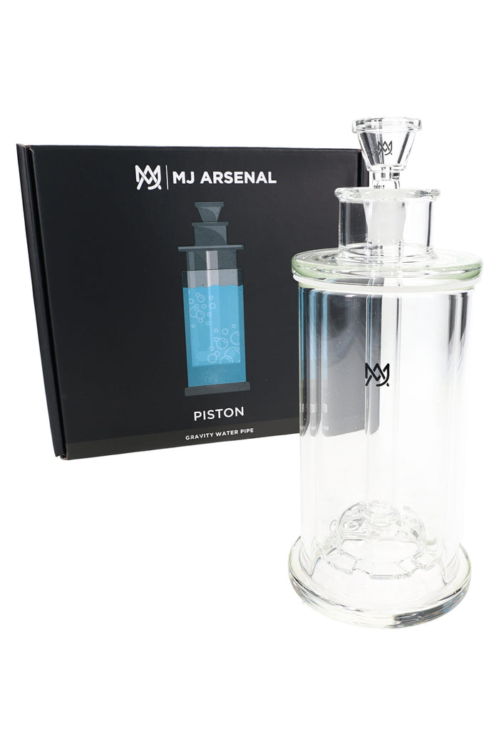 MJ Arsenal Piston gravity bong next to retail box, clear glass piston-style top and compact cylinder chamber.