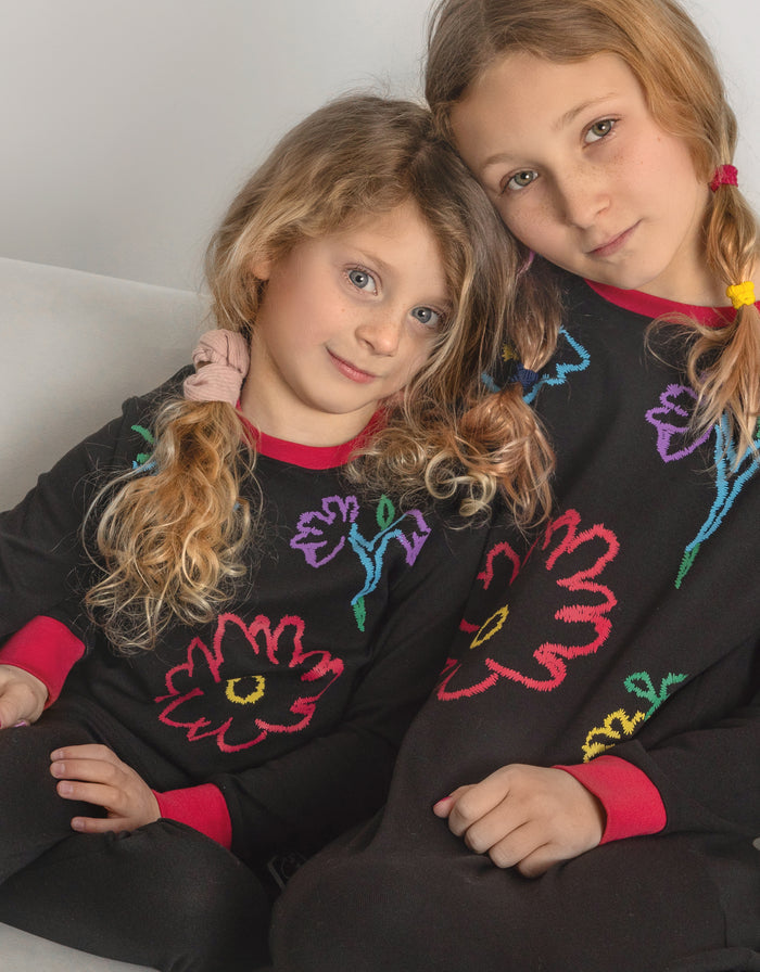 Kids black long-sleeve pajama top and leggings with fuzzy multicolor flower graphics and red cuffs