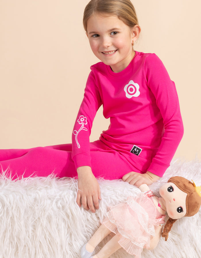Pink kids pajama legging set on child model, flower logo on long-sleeve top, elastic cuffs.