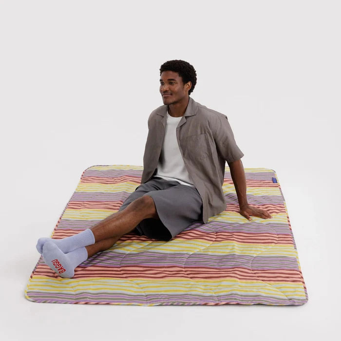 Person sitting on a colorful striped blanket against a white background